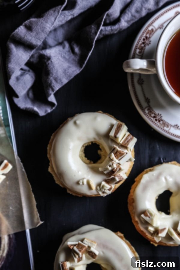 Baked White Chocolate Doughnuts with Peanut Butter Crumble 4 Three White Chocolate Baked Doughnuts adorned with generous White Chocolate Peanut Butter Crumbles on a rustic surface