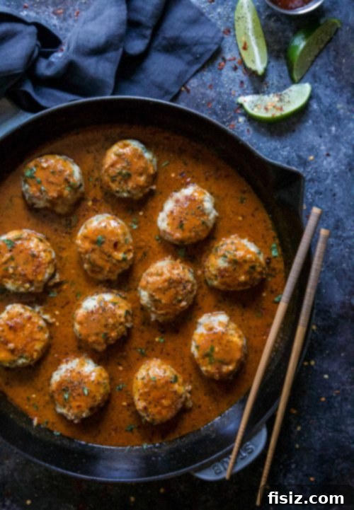 Fragrant Thai Red Curry Chicken Meatballs 4 Close-up of vibrant Thai Red Curry Chicken Meatballs simmering in a rich sauce in a cast iron skillet, garnished with fresh herbs.