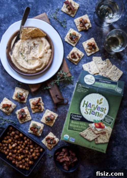 Autumn Pumpkin Hummus with Crispy Spiced Chickpeas and Smoky Sage Bacon 4 A top-down view of the Pumpkin Hummus appetizer spread, showcasing the vibrant orange dip surrounded by an array of Harvest Stone crackers and a serving spoon, ready for guests.