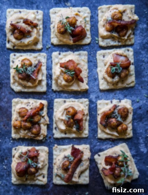 Autumn Pumpkin Hummus with Crispy Spiced Chickpeas and Smoky Sage Bacon 5 A close-up of a Harvest Stone Cracked Pepper cracker topped with a dollop of Pumpkin Hummus, spiced chickpeas, and a piece of sage bacon, ready to be enjoyed.