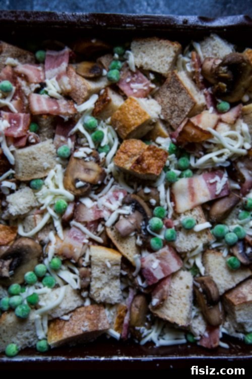 Close-up shot of the unbaked Bacon, Burrata & Smoked Mozzarella Strata mixture with bread cubes, crispy bacon, and creamy burrata peeking through.