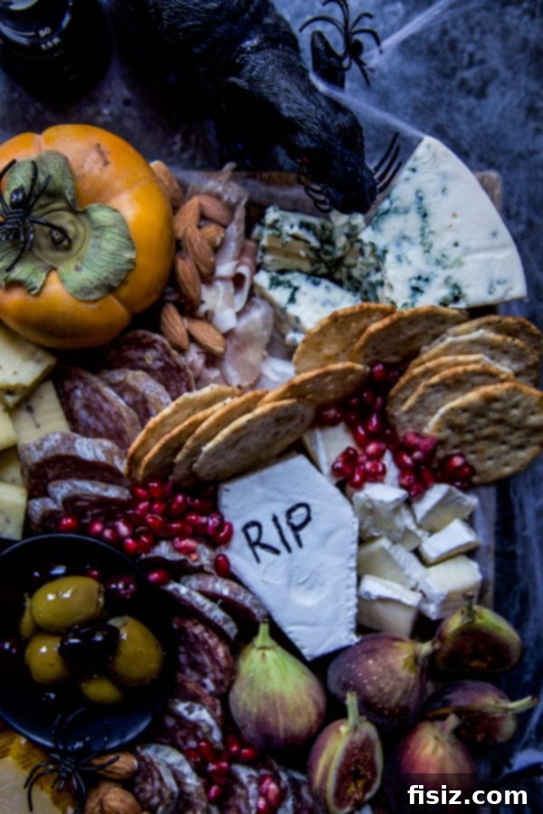 Crafting a Killer Halloween Charcuterie Board 4 Close up of a Halloween charcuterie board showcasing a small decorative gourd, an assortment of cured meats, various gourmet cheeses, a selection of crackers, and scattered pomegranate seeds, all contributing to a dark and autumnal party theme.
