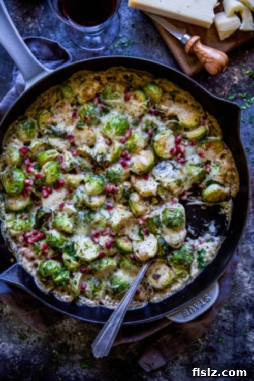 Close-up of golden brown Brussels sprouts baking in a skillet with melted cheese and pomegranate seeds.