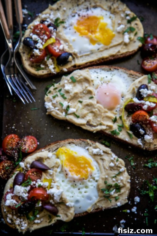 Mediterranean Egg Nest Toast with Hummus 6 Appetizing Mediterranean Egg-in-a-Hole Toast with various fresh toppings on a wooden serving board