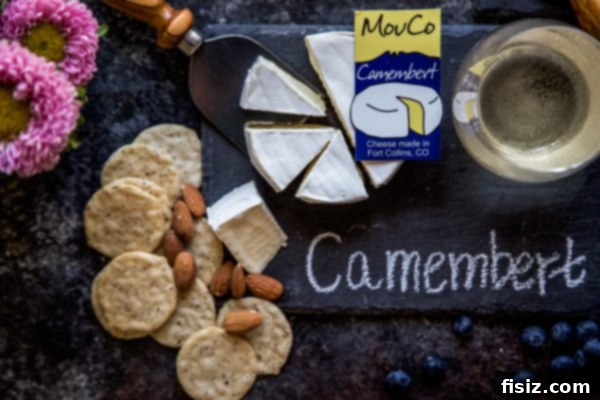 MouCo Cheese And Wine Pairing 8 A traditional wheel of MouCo Camembert cheese, with a portion cut to reveal its soft, creamy texture, accompanied by a glass of Pinot Gris.