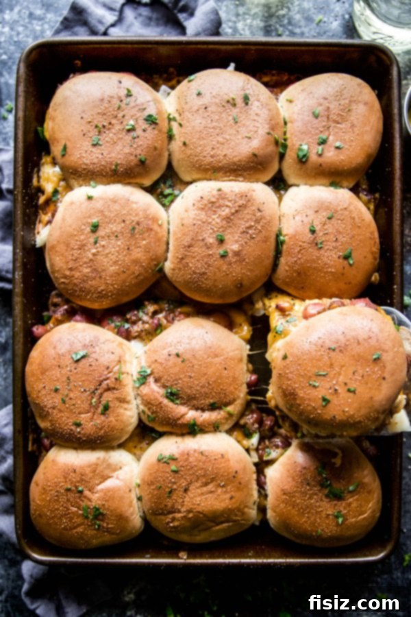Baked Chili Cheese Dog Sliders 6 A hand reaching for a Chili Cheese Dog Baked Slider from a casserole dish