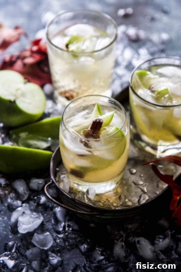 Spiced Apple Ginger Spirit 2 Three glasses of Apple Ginger Cocktail, garnished with green apple slices and cinnamon sticks, on a rustic wooden surface, exuding a cozy fall vibe.
