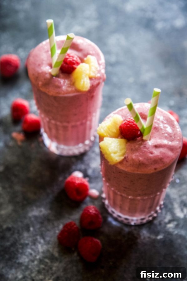 Tropical Raspberry Mango Protein Fuel 5 A tall glass of Raspberry Mango Protein Smoothie garnished with fresh raspberries and a slice of mango, ready to be enjoyed.
