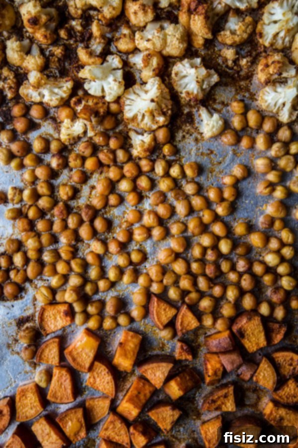Vibrant Roasted Veggie Shawarma Bowls 4 Freshly chopped sweet potatoes, cauliflower florets, and chickpeas tossed with olive oil and shawarma spices on a baking sheet, ready for roasting.