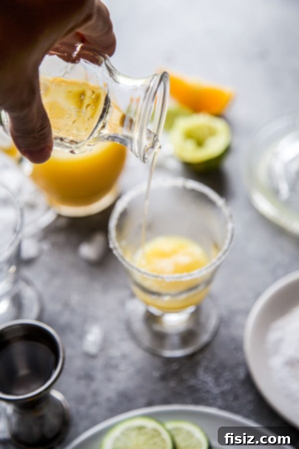 Sparkling Orange Tequila 5 A Mimosa Margarita with a salted rim and orange slice garnish, on a light background.