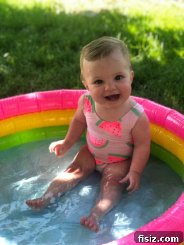 Nine Months of Life with Charlie 11 A baby girl with a pink swimsuit and hat, happily playing in a small pool.