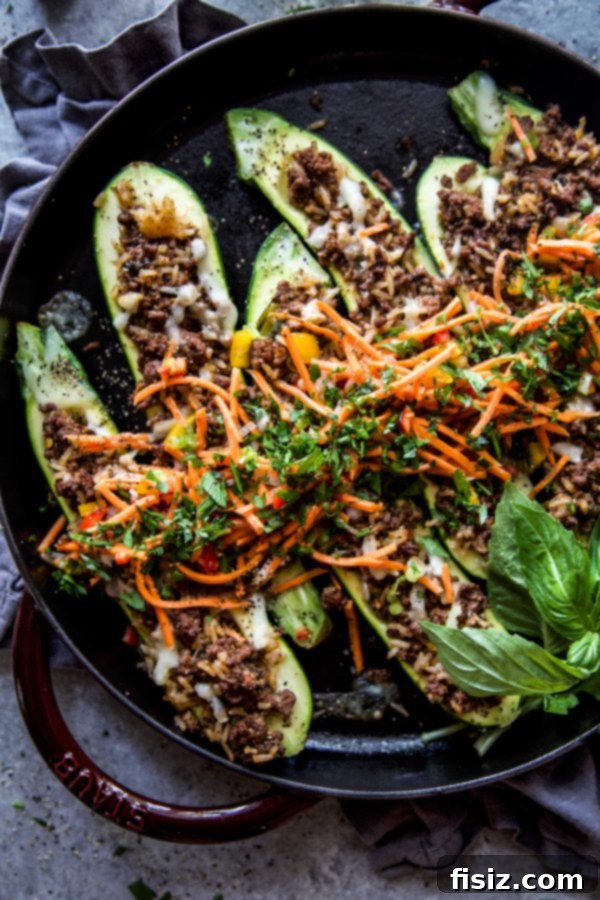 Thai Basil Beef Zucchini Boats 3 Two halves of Thai Basil Beef Stuffed Zucchini boats on a plate, garnished with fresh herbs and a red pepper topping.