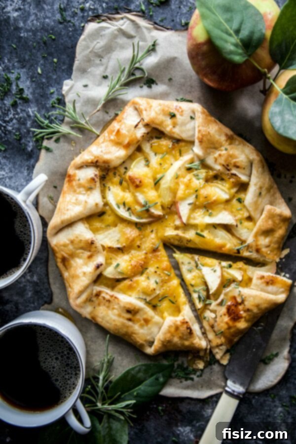 Honeycrisp Tart with Sharp Cheddar and Rosemary Honey 2 Honeycrisp Tart with Cheddar and Rosemary Honey on a rustic wooden board, garnished with fresh rosemary sprigs.