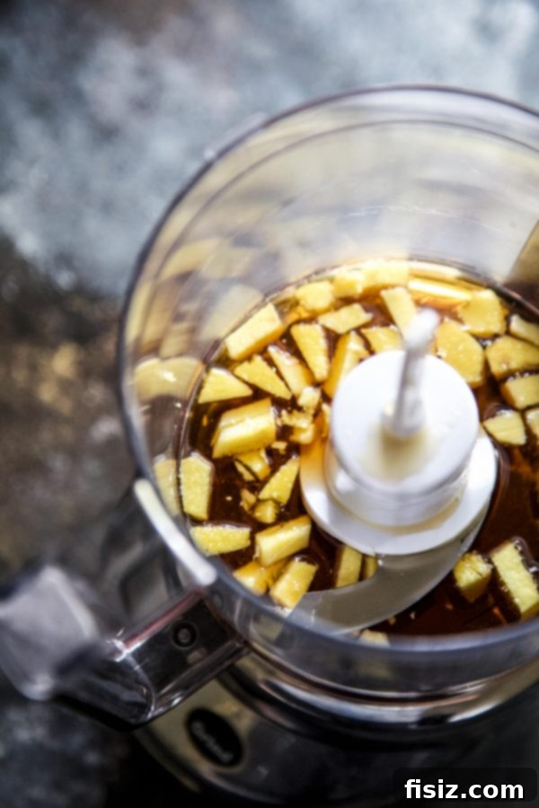 Ingredients for Apple Bourbon Ginger Spritz laid out on a wooden surface, including fresh ginger, maple syrup, bourbon, and apple cider