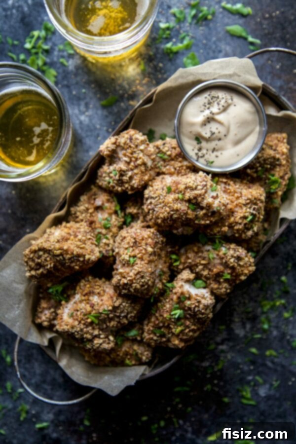 Spiced Pecan Chicken Bites & Chipotle Mustard Dip 3 Close-up of golden Spiced Pecan Baked Chicken Nuggets on a white plate, garnished with fresh herbs.
