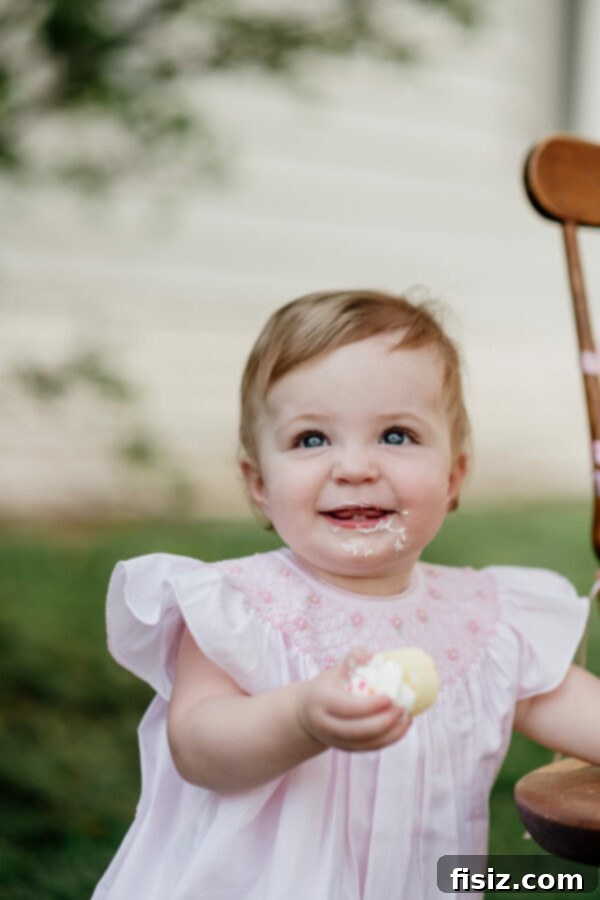 Our First Year with Charlie 2 A baby girl, Charlie, smiling while sitting in a high chair, celebrating her first birthday with a mini cupcake.