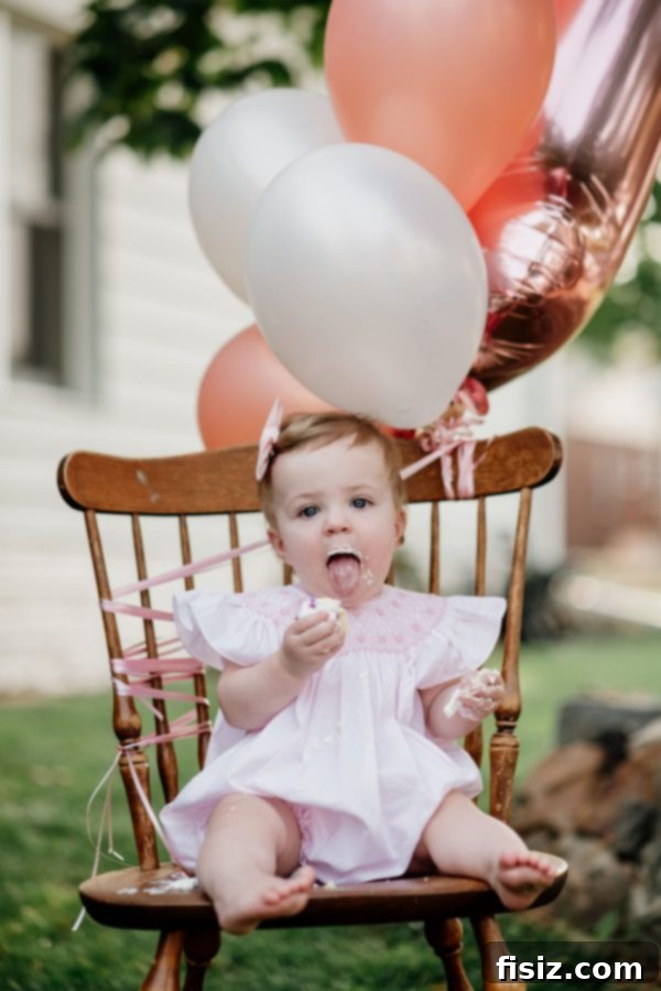Our First Year with Charlie 9 Charlie enjoying her first birthday mini cupcake during a professional photoshoot, surrounded by festive balloons.