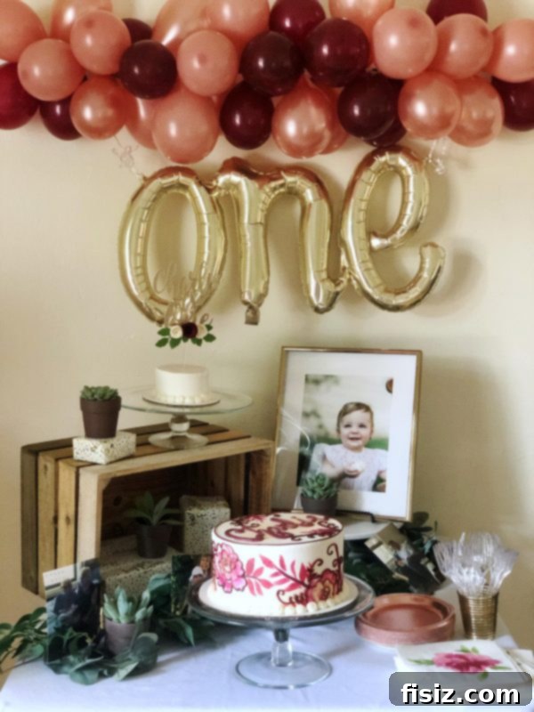 Our First Year with Charlie 10 Close-up of elegant party decorations including a balloon banner and other themed elements in pink, burgundy, and gold.