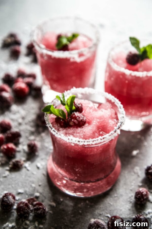 Mistletoe Kiss Margaritas 2 Vibrant cranberry margarita garnished with sugared cranberries on a rustic board, perfect for holiday celebrations. Easy Mistletoe Margaritas.