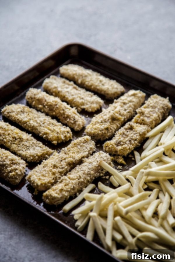 Zaatar Crusted Fish and Chips 5 Uncooked Baked Za'atar Fish Sticks and Frozen French Fries laid out on a baking sheet, ready for the oven.