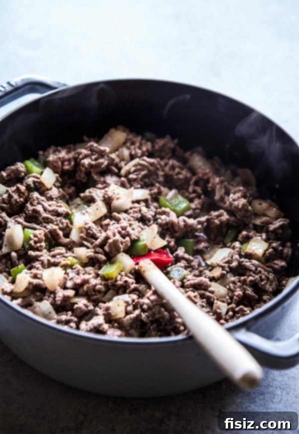 Sautéing ground beef, green pepper, and onion in a skillet for the pie base