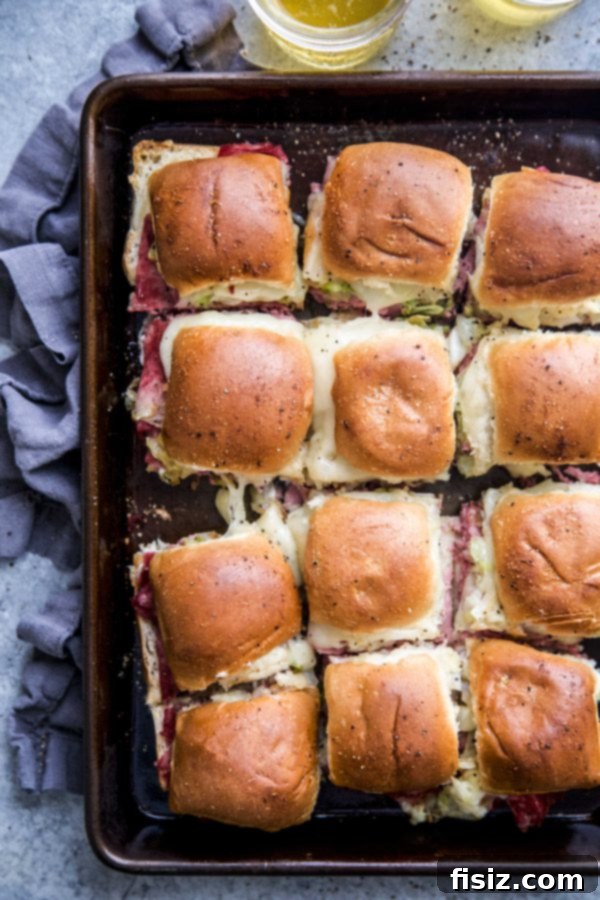 One-Pan Wonder Corned Beef Sliders 3 Overhead view of a baking sheet filled with Sheet Pan Corned Beef Sliders, layered with meat and cheese.