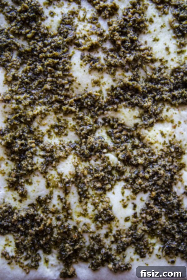 Ultimate Pesto Pepperoni Three Cheese Pizza 4 A close-up shot of vibrant green pesto being spread evenly over a pizza crust.