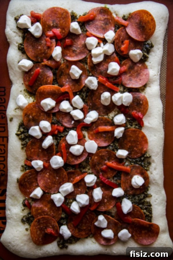 Ultimate Pesto Pepperoni Three Cheese Pizza 5 Uncooked Three Cheese Pesto Pepperoni Pizza, ready to be baked, showcasing the organized toppings.