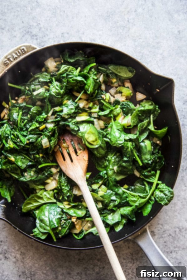 Green Shakshuka with Feta, Spinach, and Peas 5 Wilted spinach cooking in a skillet with other vegetables