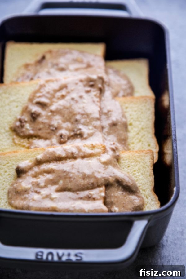 Baked French Toast with Nut Butter and Bananas 5 The creamy nut butter and cream cheese mixture being spread over a layer of brioche bread slices in a baking dish