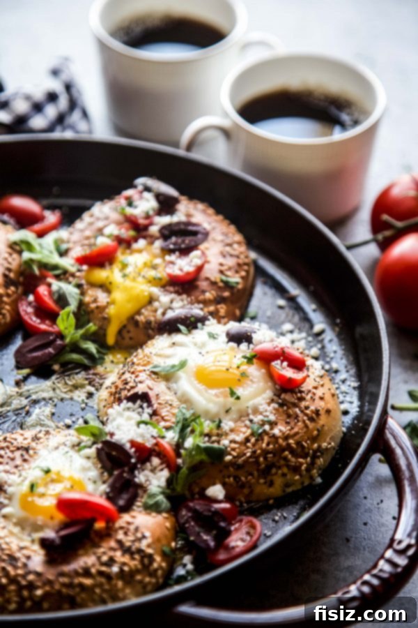 Two halves of egg stuffed Greek bagels on a white plate with fresh ingredients