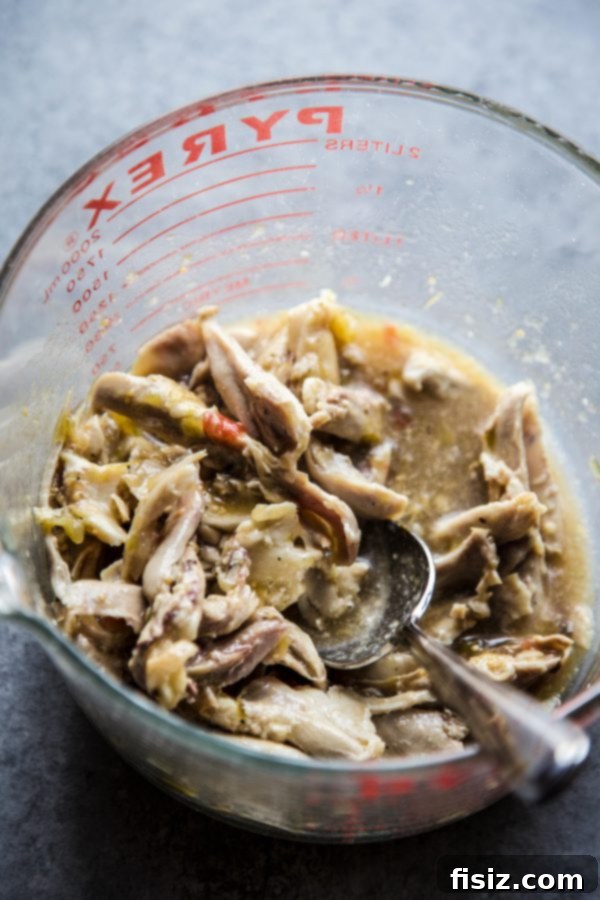 Ultimate Sheet Pan Verde Chicken Nachos 4 Shredded chicken generously mixed with vibrant green salsa verde in a white bowl.