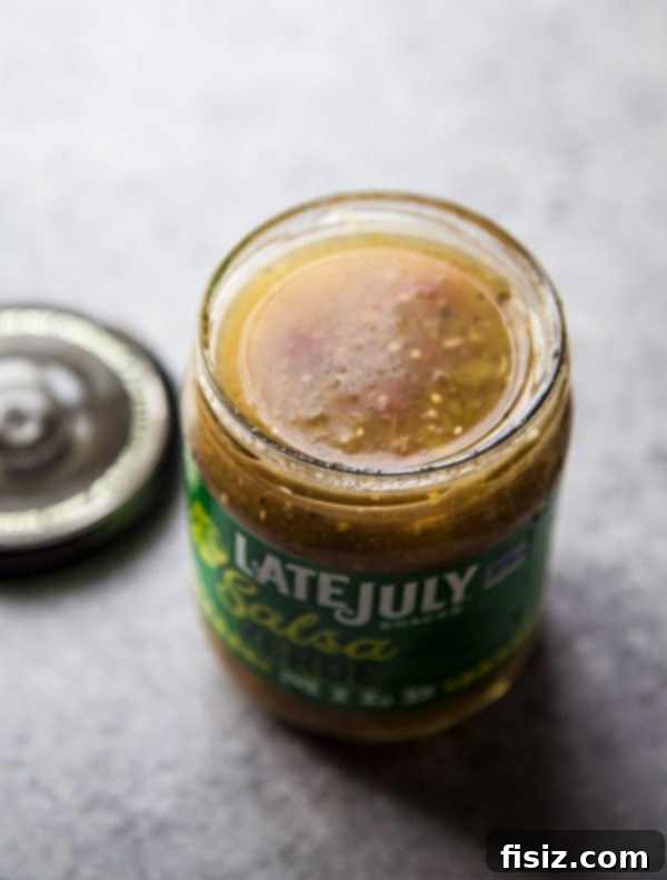 Ultimate Sheet Pan Verde Chicken Nachos 5 A glass jar of bright green salsa verde on a rustic wooden surface.