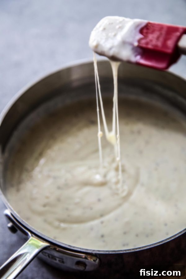 Guilt-Free Cheesy Zucchini Gratin 4 Cheese sauce in a skillet, dripping from a spatula.