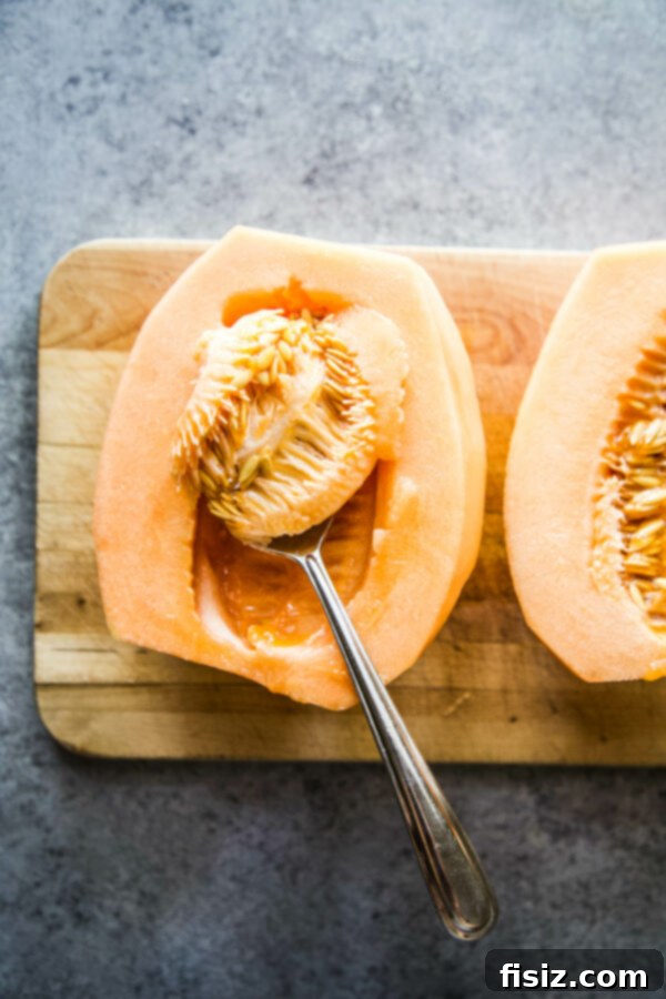 Savory Melon Crunch 6 Halved cantaloupe with seeds and membranes being scooped out, demonstrating proper preparation.