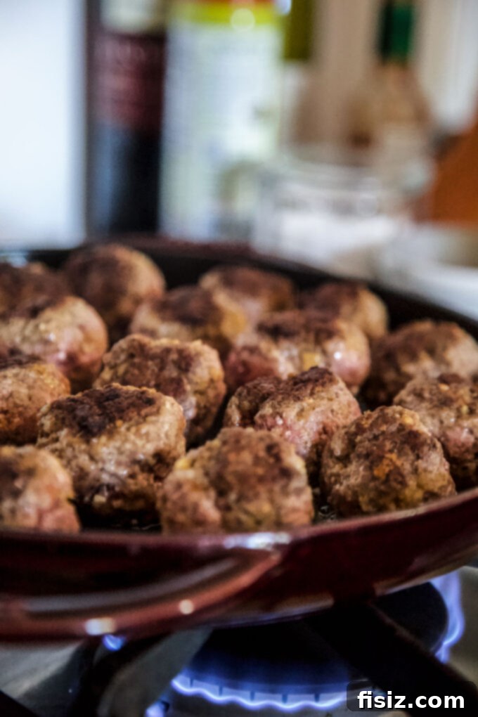 Caramelized Apple Beef Meatballs 5 Beef meatballs sizzling and browning in a hot cast iron skillet, developing a delicious crust.