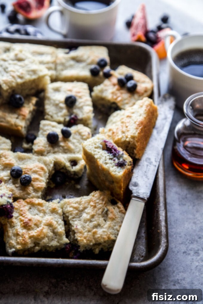 Close-up of freshly baked Blueberry & Blood Orange Sheet Pan Pancakes on a baking sheet, showcasing the vibrant fruit and fluffy texture.