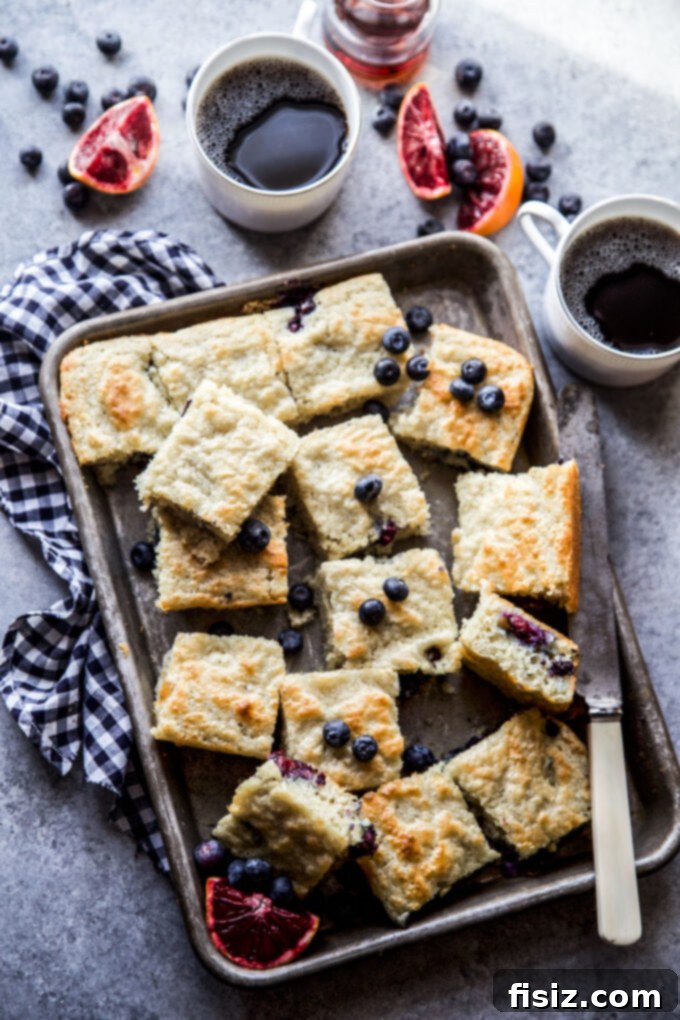 A close-up shot of a single slice of Blueberry & Blood Orange Sheet Pan Pancake, drizzled with maple syrup.
