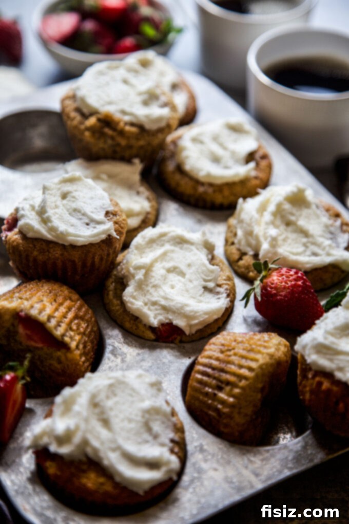 Two freshly baked Strawberry Banana Bread Muffins with generous vanilla frosting