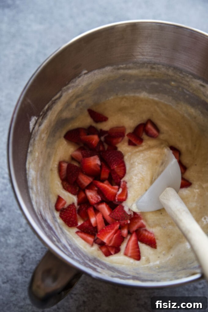 Close-up view of muffin batter being mixed with diced fresh strawberries