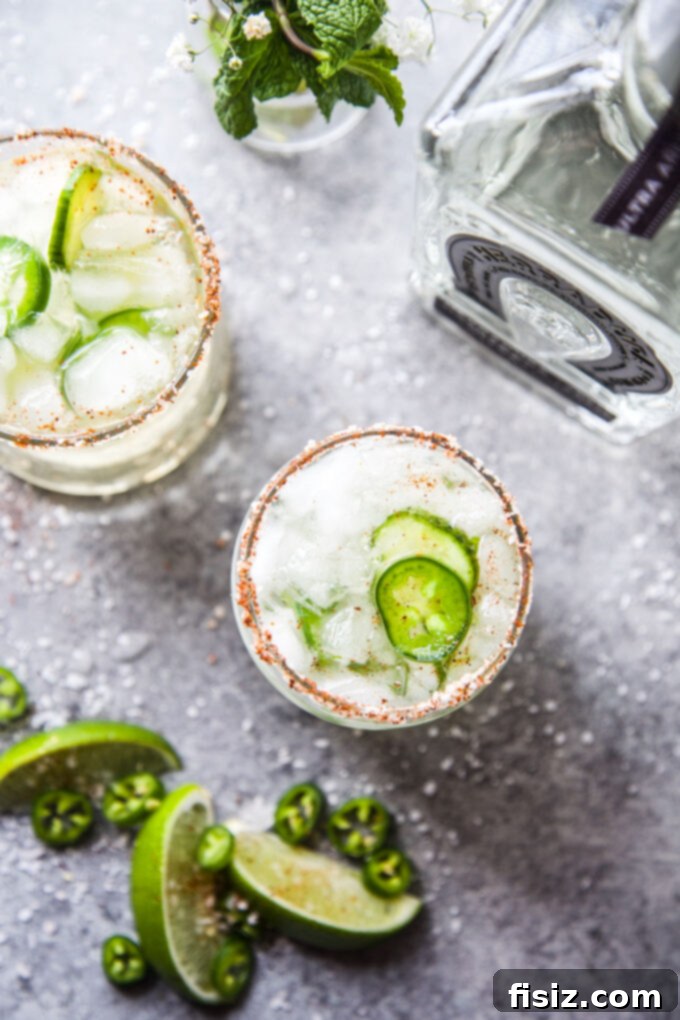 Cucumber Margarita with a Tequila Lime Jalapeño Zing 7 Two glasses of Spicy Cucumber Margarita with pickled jalapenos and lime slices, enjoyed on an outdoor setting.