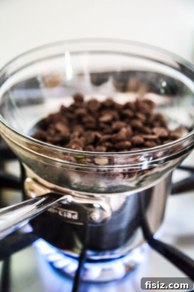 Wicked Good Halloween Dark Chocolate Peanut Butter Cups 4 Close-up of dark chocolate chips melting gently in a bowl over a saucepan, demonstrating the double boiler method for homemade peanut butter cups.