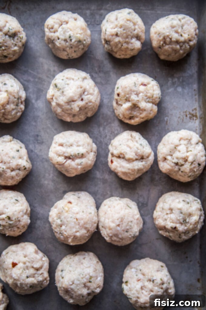 Zesty Lemon Garlic Chicken Meatballs with Creamy Hummus 5 Raw, formed chicken meatballs uniformly arranged on a baking sheet, ready for cooking.
