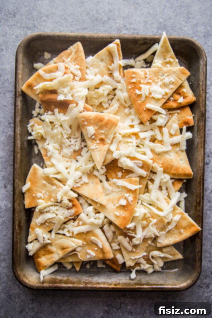 Loaded Beef Pita Nachos with Whipped Feta 6 Pita triangles on a baking sheet, generously covered with a layer of shredded mozzarella and provolone cheese, ready for the oven.