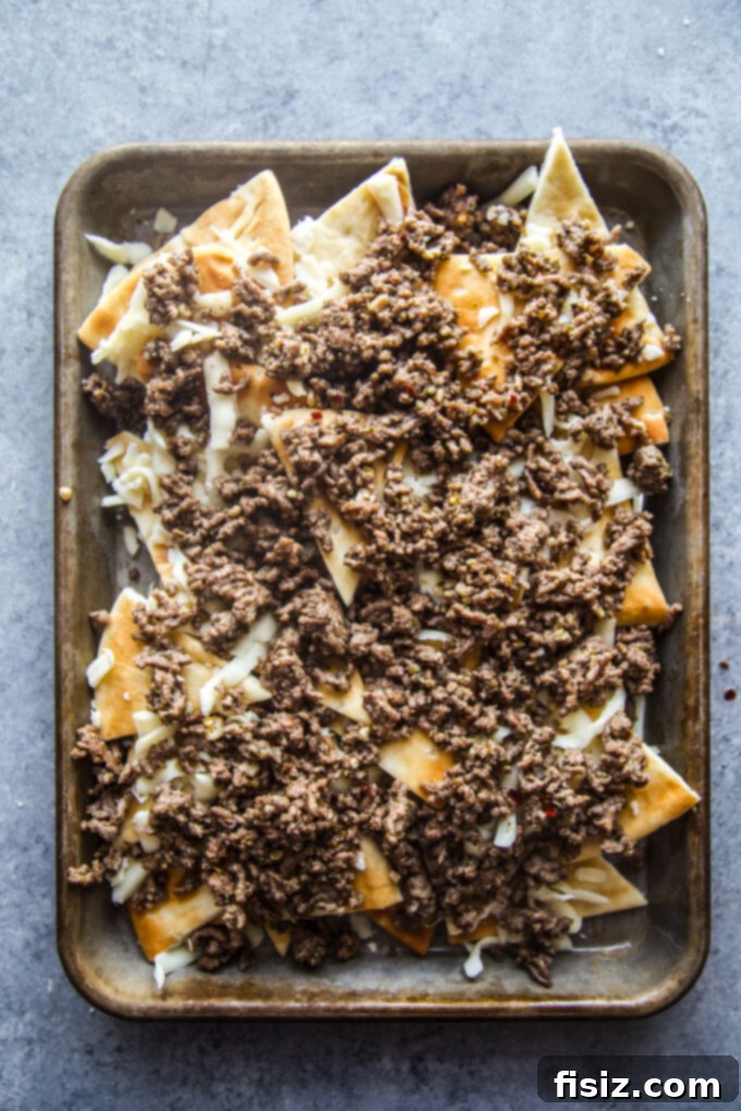 Loaded Beef Pita Nachos with Whipped Feta 7 Pita chips covered with melted shredded cheese and a savory layer of seasoned ground beef, creating the base for the ultimate nachos.