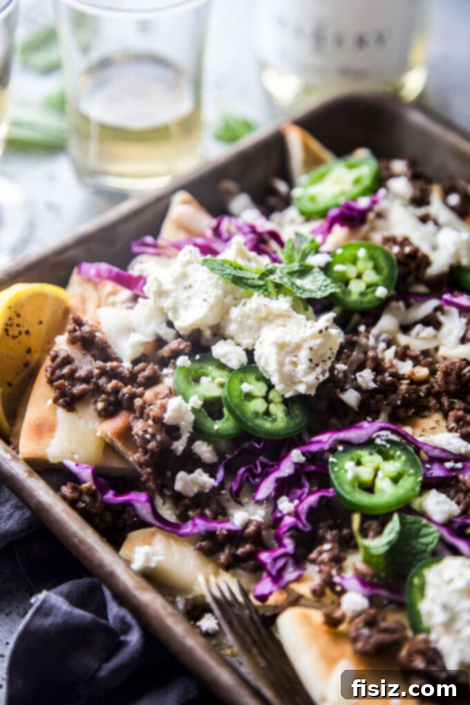 Loaded Beef Pita Nachos with Whipped Feta 9 A top-down shot of a large sheet pan filled with golden Beef Pita Nachos, generously topped with melted cheese, savory beef, and fresh, vibrant garnishes including whipped feta.