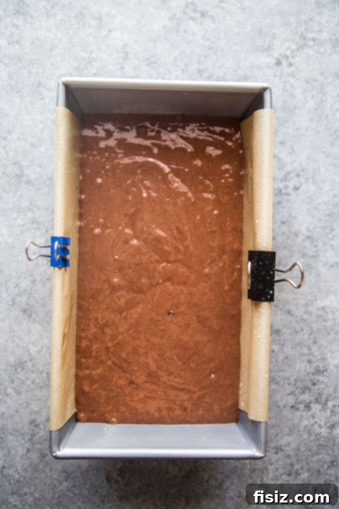 Smooth chocolate cake batter poured into a meticulously prepared loaf pan, ready to be baked.