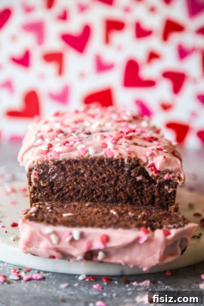 Beautifully garnished chocolate loaf cake with cherry frosting and festive heart sprinkles, perfect for any celebration, from www.thecuriousplate.com