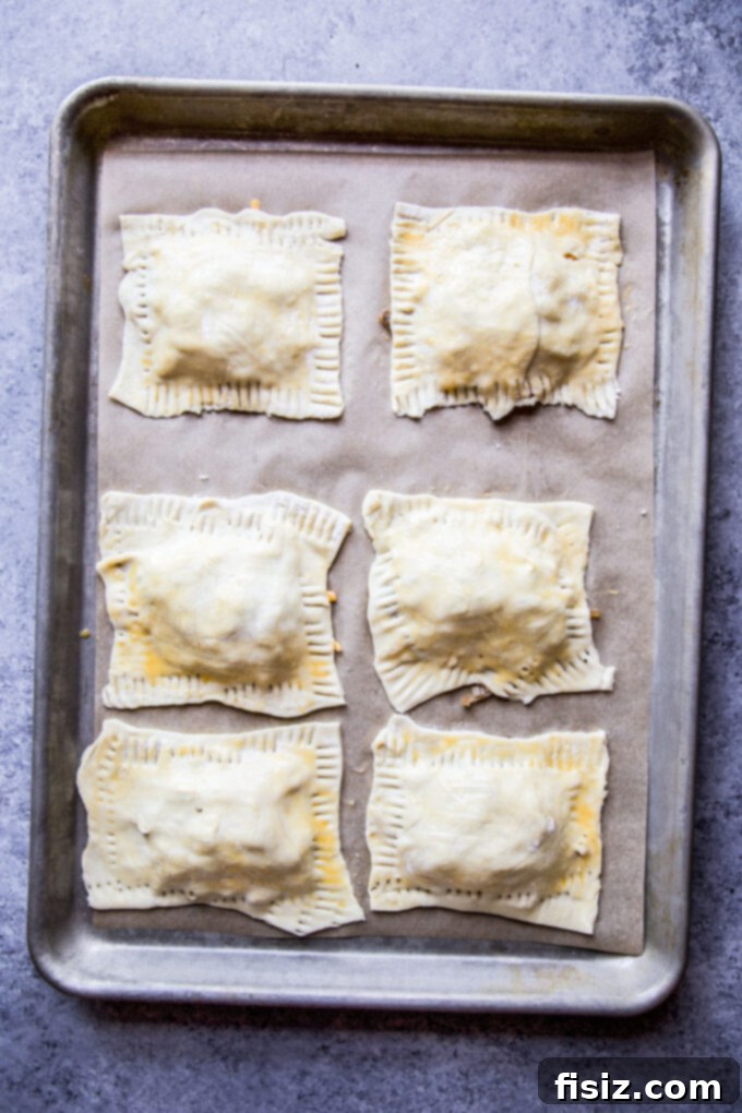 Apple, cheddar, and caramelized rum onion mixture covered with puff pastry rectangles on a baking sheet