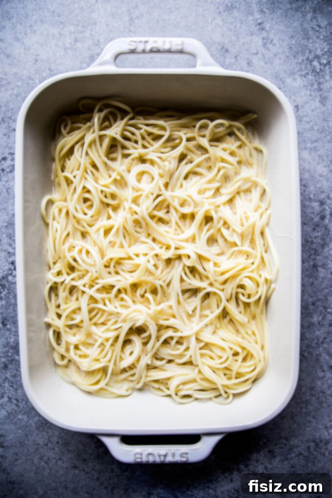 Creamy Baked Alfredo Spaghetti 4 A casserole dish filled with cooked spaghetti, ready to be topped with sauces and cheese for baking.